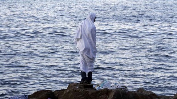 A migrant wrapped in a white a blanket stands on the rocks of the seawall at the Saint Ludovic border crossing on the Mediterranean Sea between Vintimille, Italy and Menton, France, June 17, 2015. REUTERS/Eric Gaillard