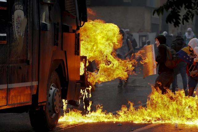 An anti-government protester wearing a Guy Fawkes mask stands with a shield near flames from molotov cocktails thrown at a water cannon by anti-government protesters during riots in Caracas in this April 20, 2014 file photo.  REUTERS/Jorge Silva/Files