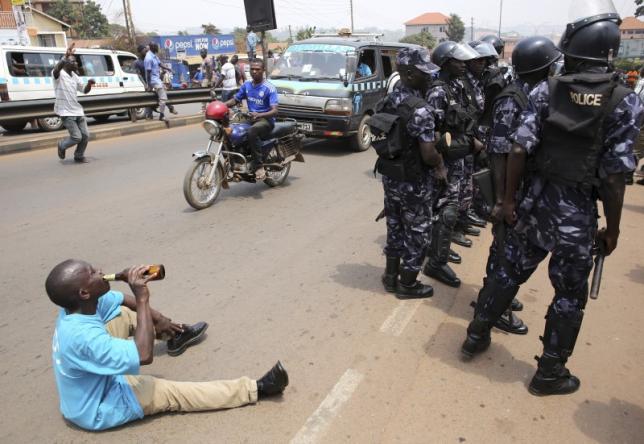 A supporter of opposition leader Kizza Besigye drinks beer in front of riot policemen in Kampala, Uganda. REUTERS/Goran Tomasevic
