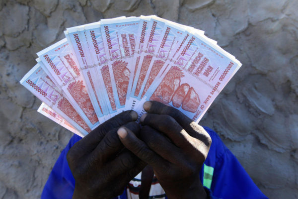 A man holds a handful of 5 Billion Zimbabwean dollar notes, in Harare, Friday, June, 12, 2015. Zimbabwe's central bank says banknotes from its old currency, which collapsed and was discarded years ago because of runaway inflation, can be exchanged for American dollars. But 100 trillion Zimbabwean dollars will fetch only 40 U.S. cents. That's a fraction of what collectors have been paying for the notes with numerous zeroes for years. (AP Photo/Tsvangirayi Mukwazhi)