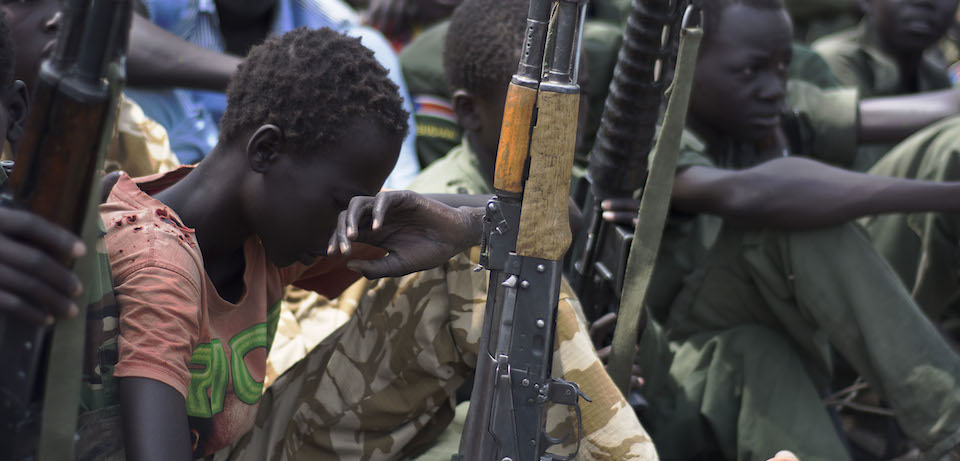 Young boys, children soldiers sit on February 10, 2015 with their rifles at a ceremony of the child soldiers disarmament, demobilisation and reintegration in Pibor oversawn by UNICEF and partners. UNICEF and its partners have overseen the release of another 300 children from the Cobra Faction armed group of former rebels of David Yau Yau. The children in Pibor, Jonglei State, surrendered their weapons and uniforms in a ceremony overseen by the South Sudan National Disarmament, Demobilization and Reintegration Commission, and the Cobra Faction and supported by UNICEF. They were to spend their first night in an interim care center where they will be provided with food, water and clothing. They will also have access to health and psychosocial services. AFP PHOTO/Charles LOMODONG / AFP / CHARLES LOMODONG (Photo credit should read CHARLES LOMODONG/AFP/Getty Images)