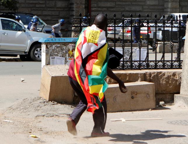 A man with a Zimbabwean flag wrapped around him throws stones at police officers during a protest against President Robert Mugabe's government's handling of the economy in Harare, Zimbabwe August 3, 2016. REUTERS/Philimon Bulawayo